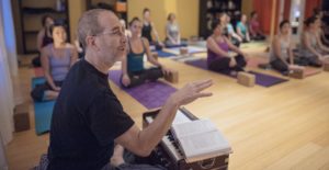 Hari-kirtana das sitting and speaking in front of a yoga class