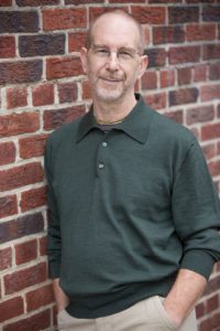 Hari-kirtana das wearing a green polo shirt leaning on a brick wall